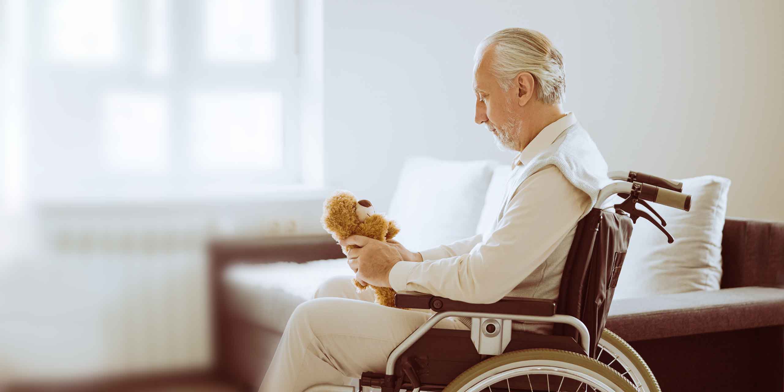 Älterer Mann im Rollstuhl schaut auf Plüschtier